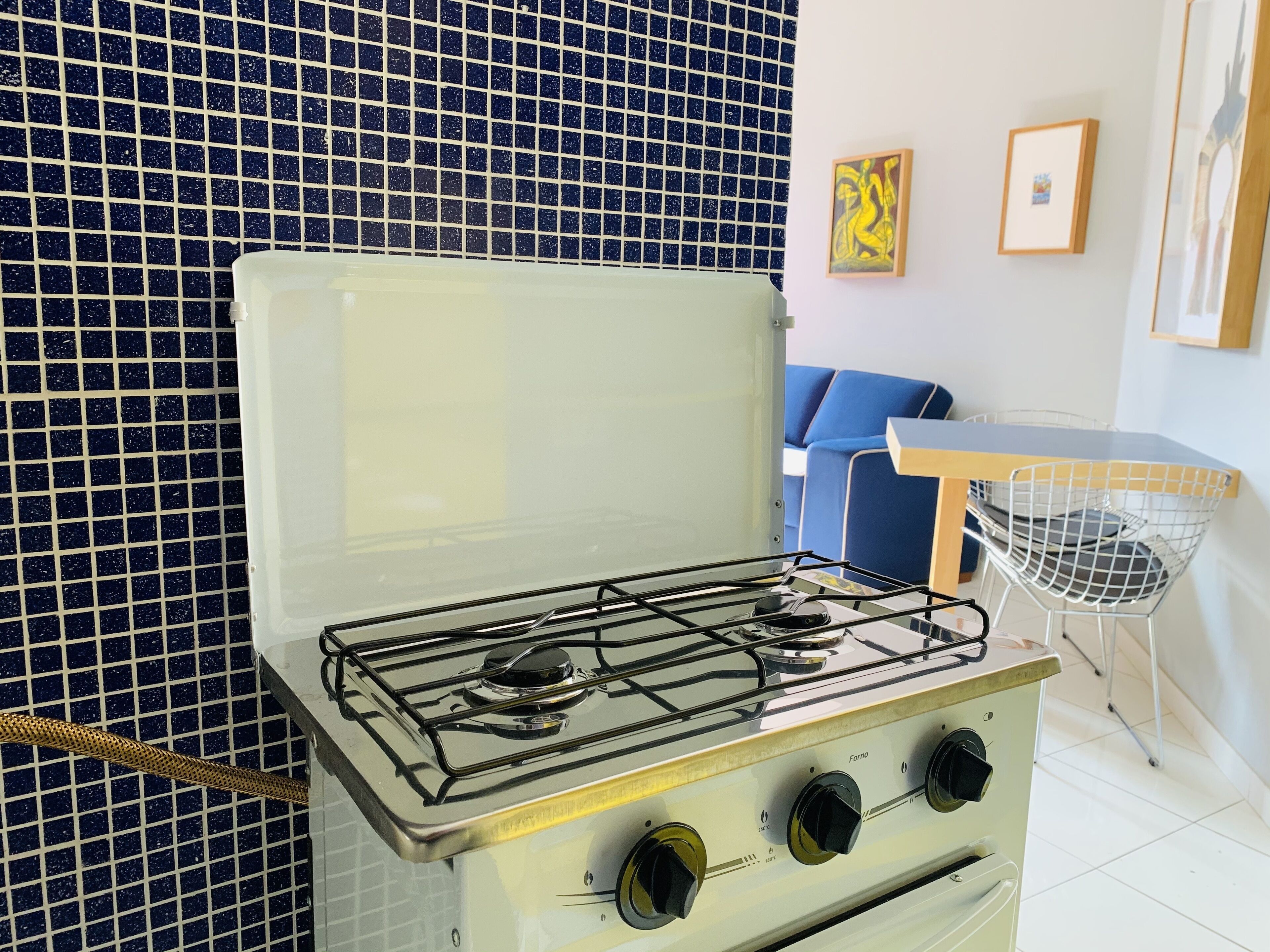 A kitchen with a white stove, a blue tiled backsplash, a blue sofa, and a small table with a chair.