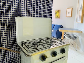 A kitchen with a white stove, a blue tiled backsplash, a blue sofa, and a small table with a chair.