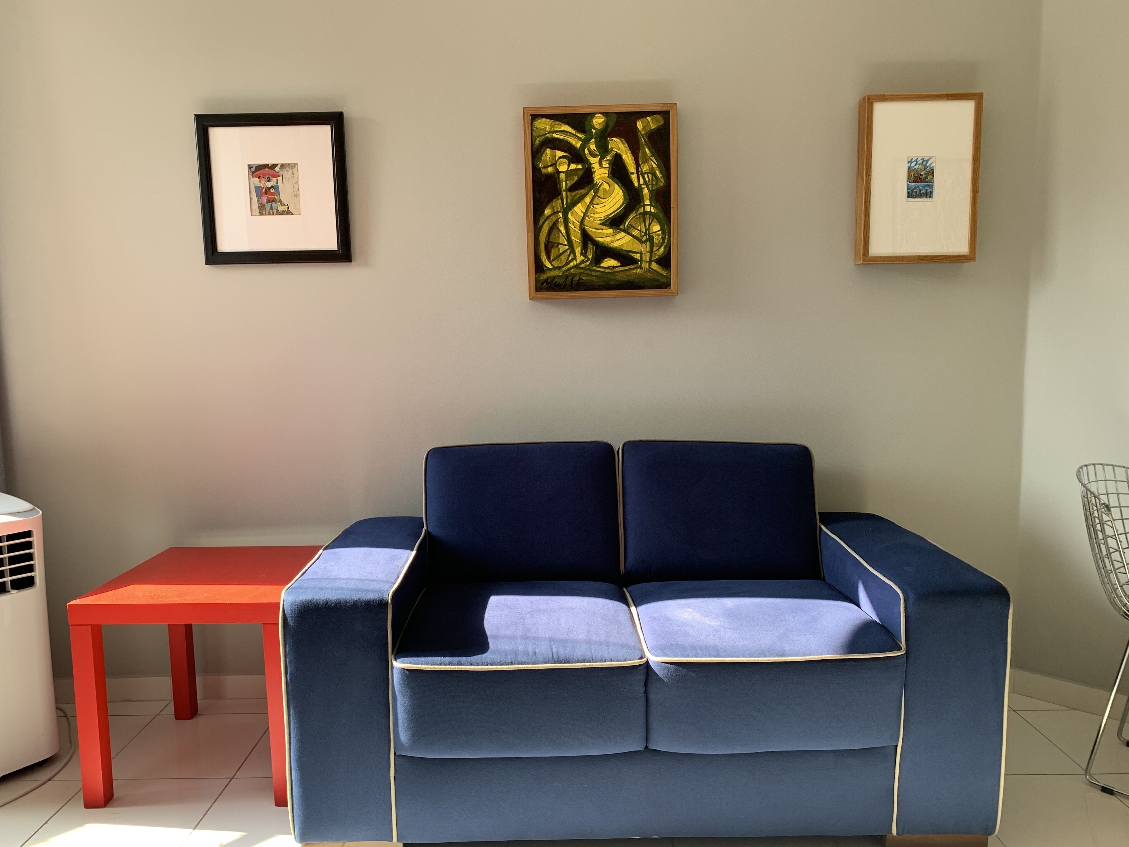 A room with a blue sofa, a red table, and framed artwork on the wall.