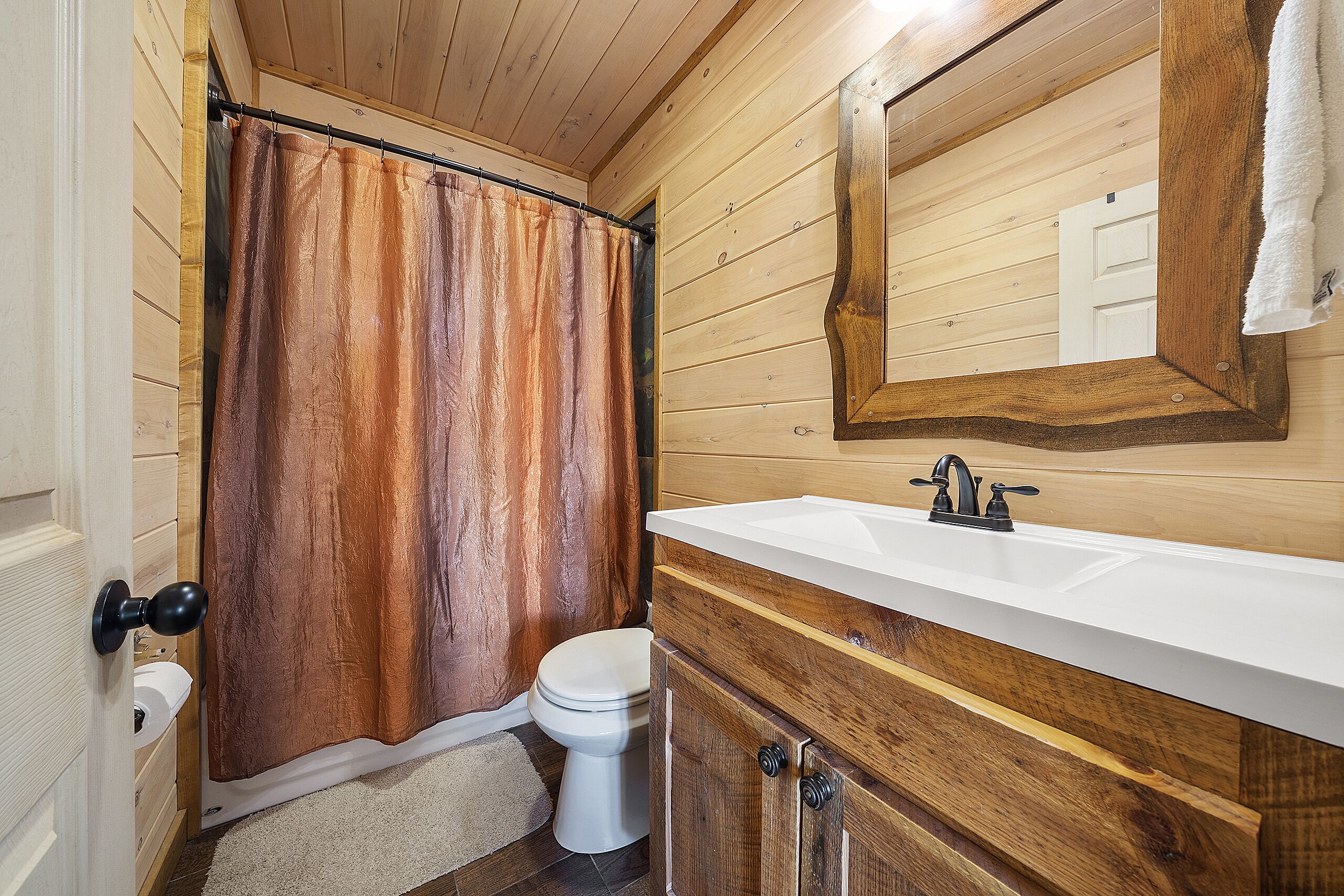 Un baño de madera con un lavamanos blanco, un armario de madera y una cortina de ducha.