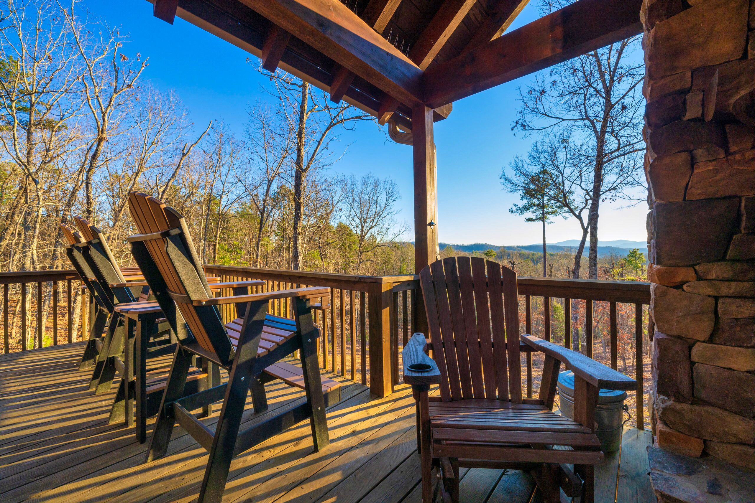 A wooden deck with Adirondack chairs and a stone wall.