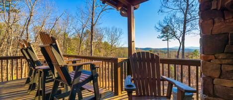 A wooden deck with Adirondack chairs and a stone wall.