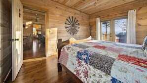 A wooden cabin bedroom with a large bed, a ceiling fan, and a view of the outdoors through a window. - NEW! Private Mountain Cabin in Gated Community w/ Mtn Views, Hot Tub & Game Room (Morganton)
