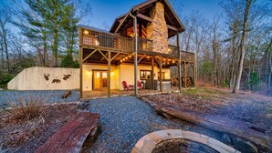 A rustic lodge with a stone fireplace, wooden deck, and deer wall art. - NEW! Private Mountain Cabin in Gated Community w/ Mtn Views, Hot Tub & Game Room (Morganton)