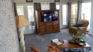 Una sala de estar con televisor, un mueble de madera, una silla, una mesa y una lámpara.