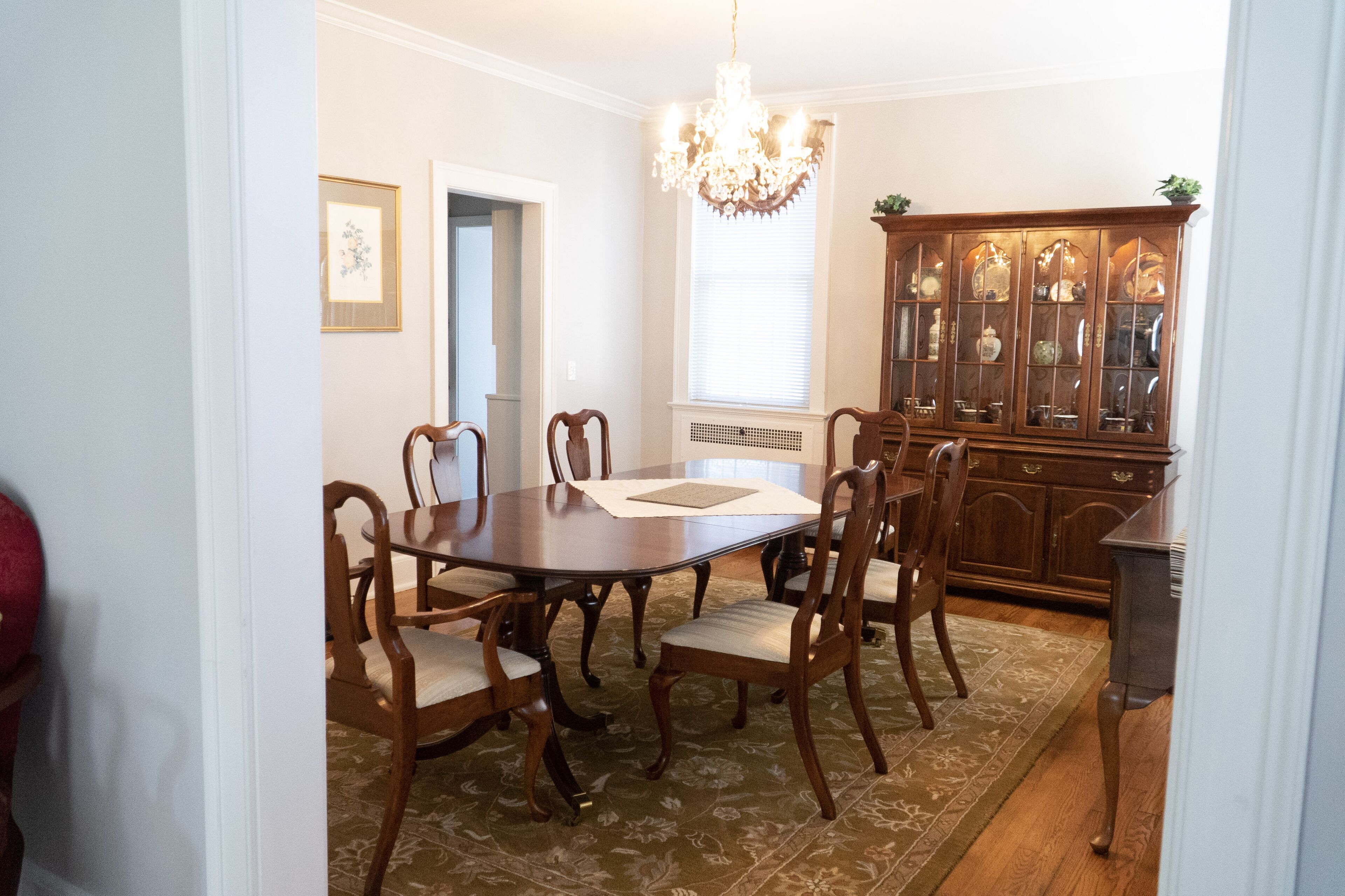 A dining room with a wooden table and chairs, a chandelier, and a china cabinet.