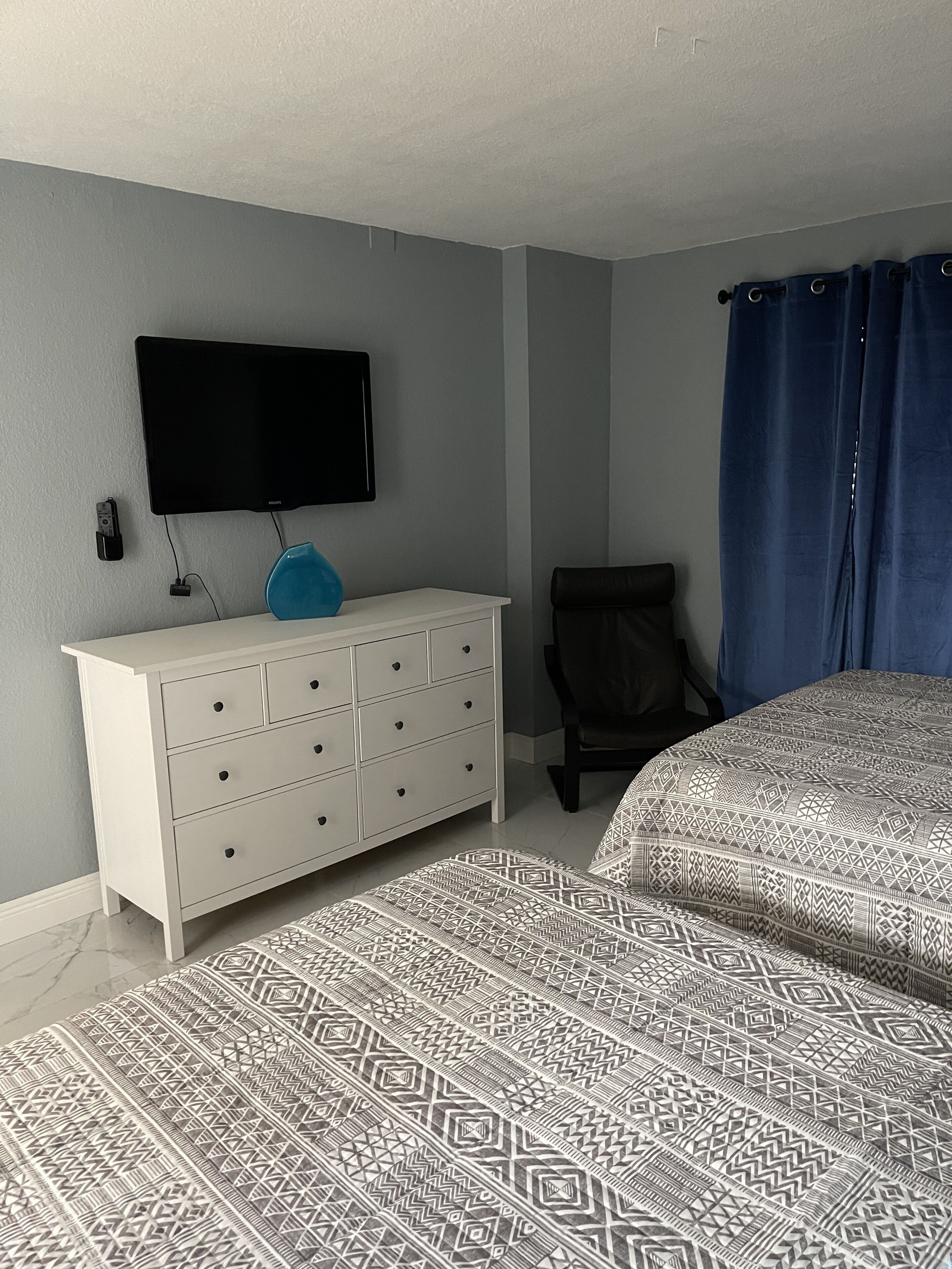 A bedroom with a bed, a dresser, a chair, a television, and a curtain.