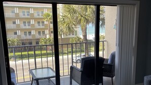 Un salon moderne avec une porte vitrée donnant sur un balcon. La pièce est dotée d’un sol en marbre, d’une table à plateau en verre et de deux fauteuils en osier.