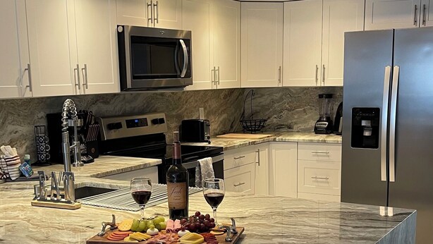 Une cuisine moderne avec des meubles blancs, un plan de travail en marbre, un réfrigérateur en acier inoxydable et une bouteille de vin.