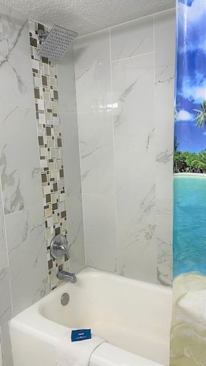 A bathroom with a bathtub, a shower, and a tiled wall with a beach mural.