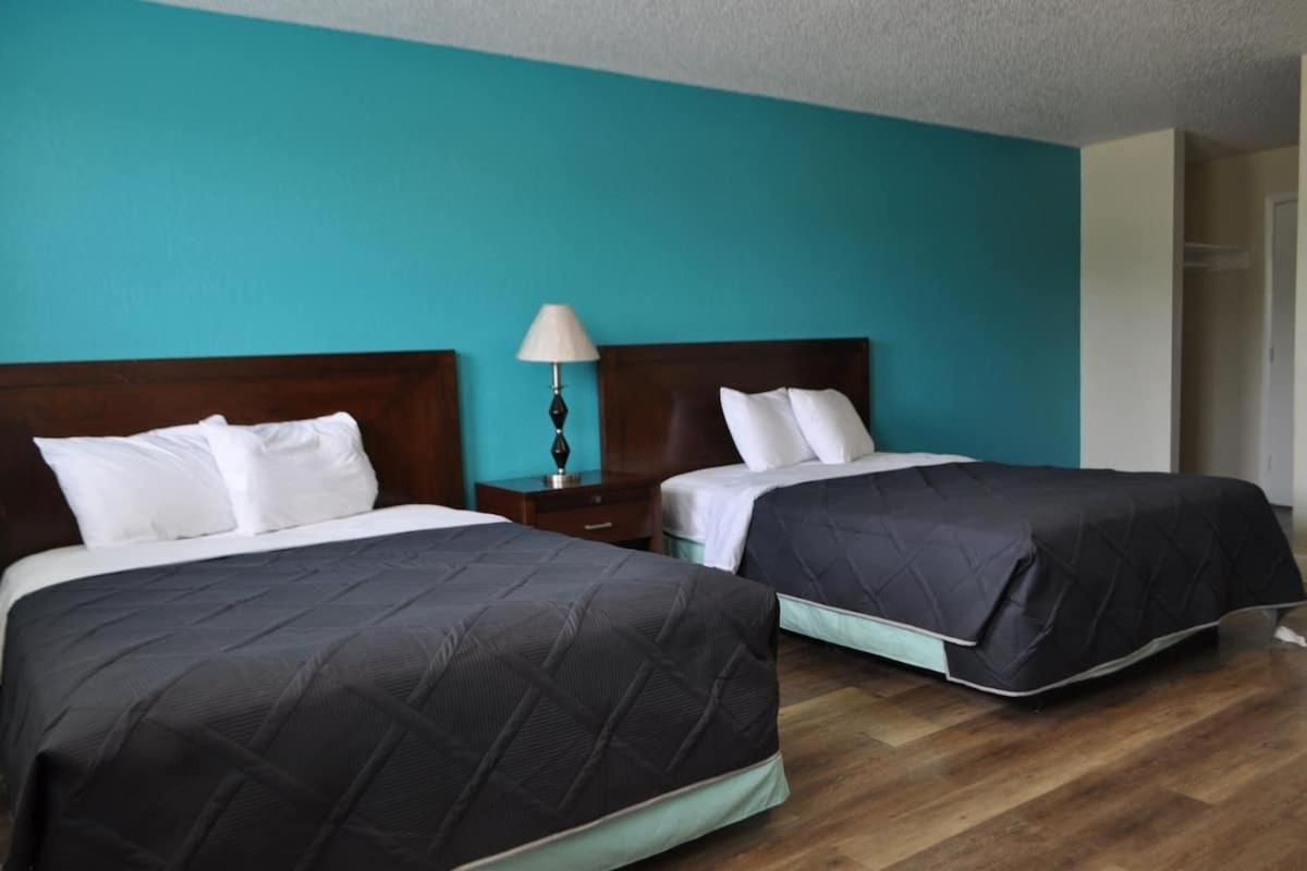 Una habitación de hotel con dos camas, una mesita de noche con lámpara y un armario.