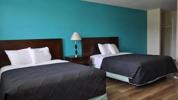 Una habitación de hotel con dos camas, una mesita de noche con lámpara y un armario.