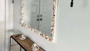 Un couloir agrémenté d’un miroir encadré de coquillages, d’une console sur laquelle sont disposés des objets décoratifs, et d’appliques murales.