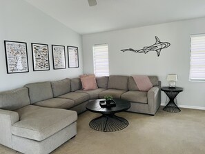Un salon moderne avec un canapé d’angle, une table basse ronde et des illustrations de poissons encadrées accrochées au mur.