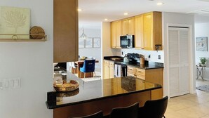 Une cuisine moderne avec des meubles en bois, un plan de travail noir et un coin repas agrémenté d’une chaise bleue.