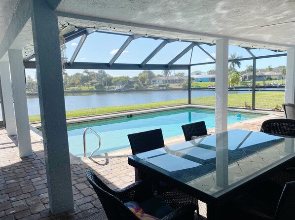 A covered outdoor area with a pool, a table, and chairs.
