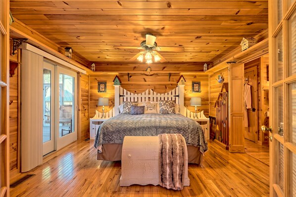 Un dormitorio de cabaña de troncos con una cama grande, techo de madera y una cerca blanca de piquetes.