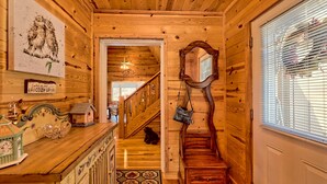 A wooden interior with a staircase, a mirror, and a small birdhouse on the counter.