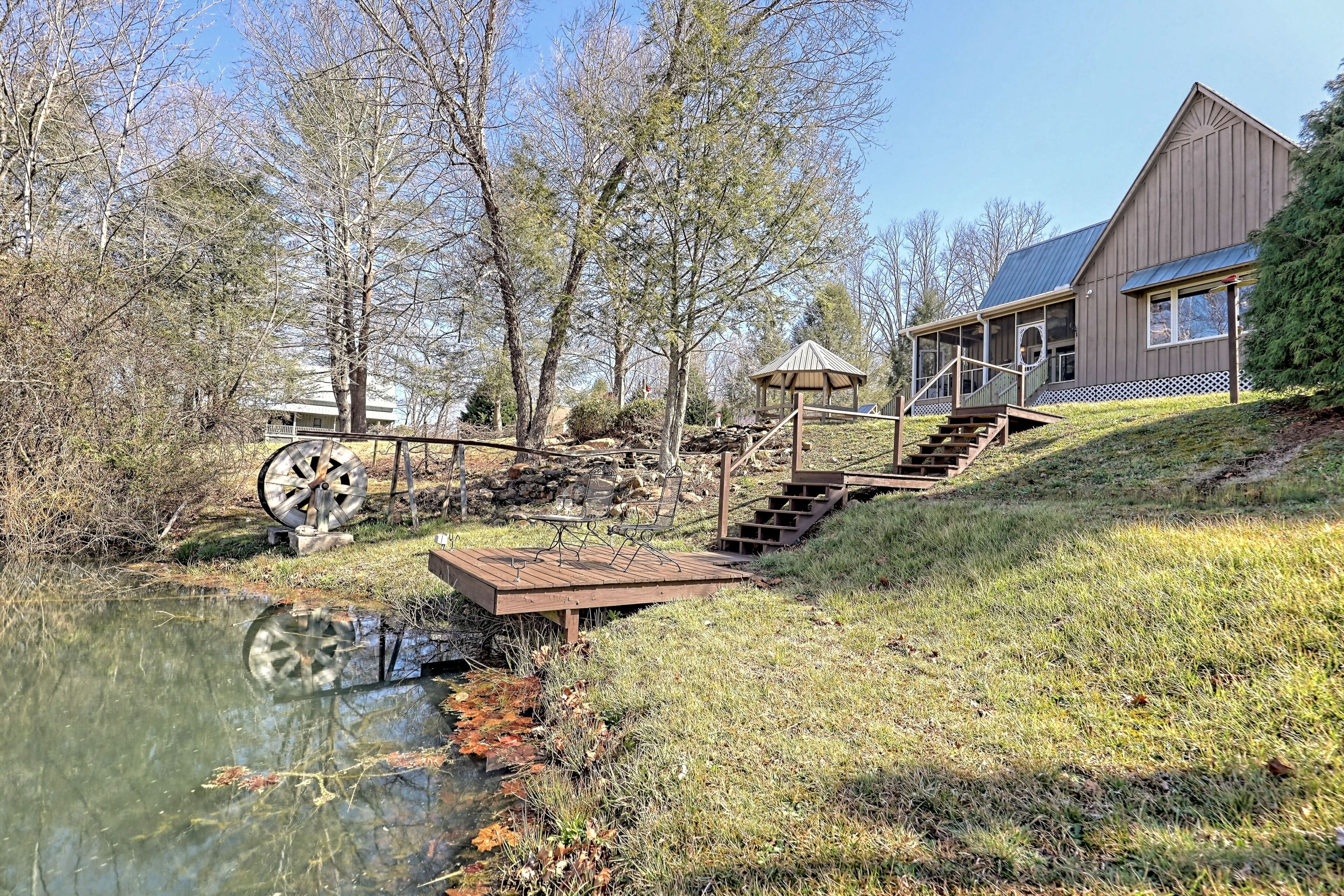 A rustic cabin with a wooden deck, a gazebo, and a pond.