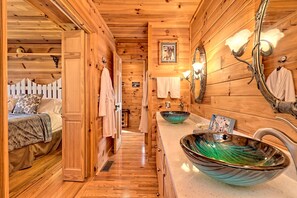 Un interior de madera con un baño, un lavabo y un recipiente decorativo, y una cama con un almohadón.