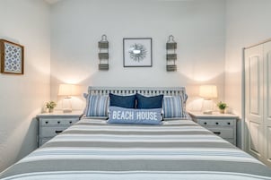 Quarto com cama, duas mesas de cabeceira, duas luminárias de parede, um quadro emoldurado e uma porta.