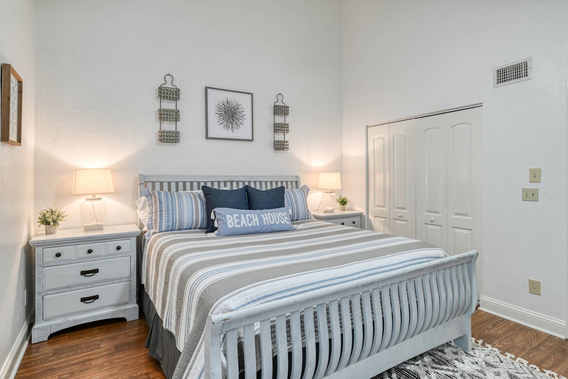 Un dormitorio con una cama, dos mesitas de noche, un tocador, una cómoda, una puerta blanca y una pared decorada.