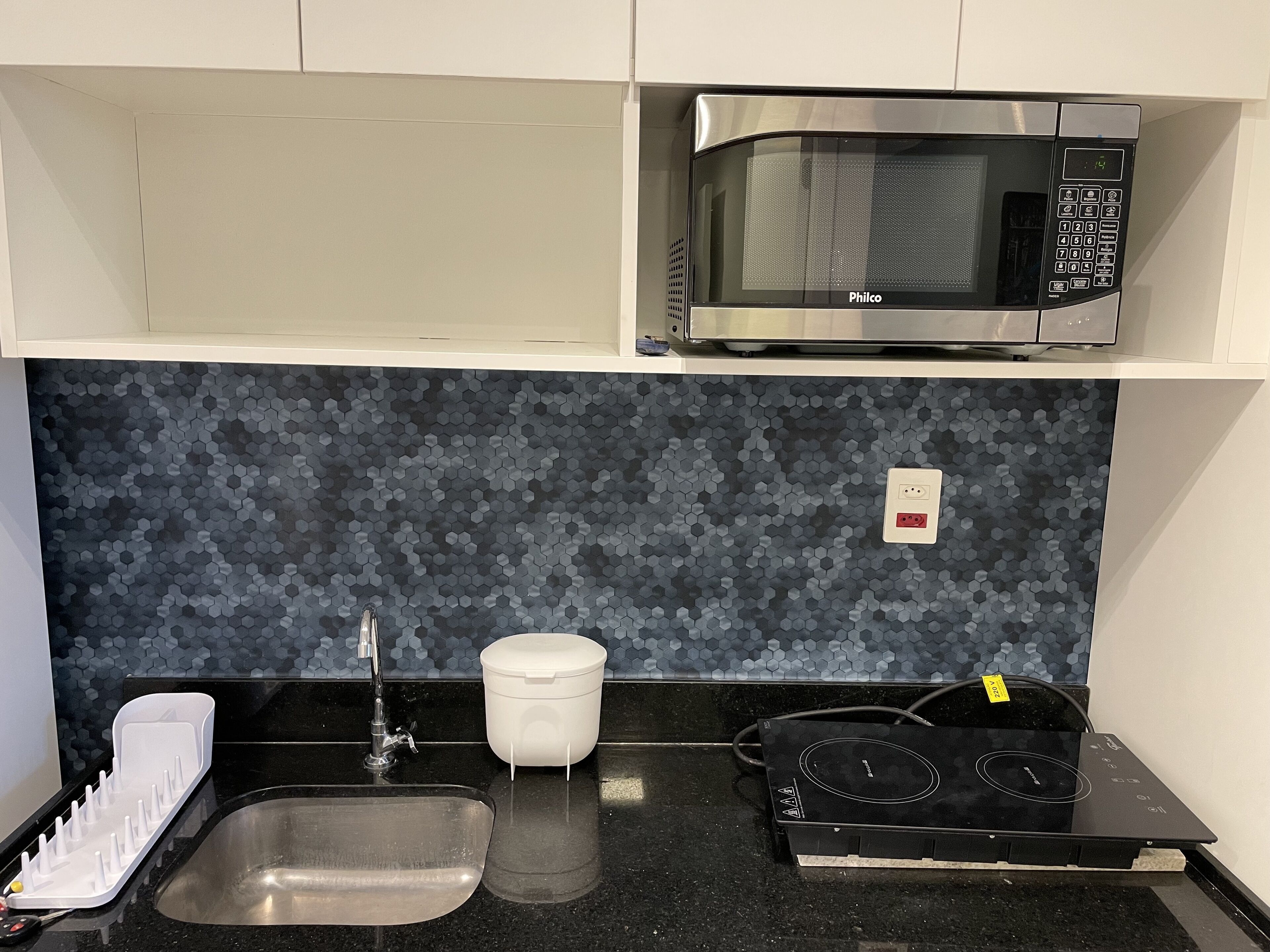 A kitchen with a microwave, sink, and induction cooktop.