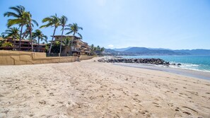 A beach with a sandy shore, palm trees, and a building with multiple balconies. - Los Tules Ocean Front Condo ,With Amazing Ocean View (Puerto Vallarta)
