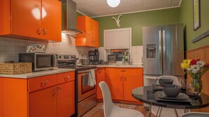 Una cocina con gabinetes naranja, un refrigerador de acero inoxidable, un microondas y una mesa de comedor con sillas.
