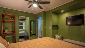 Un dormitorio con cama, ventilador de techo, televisor y ventana con cortinas.