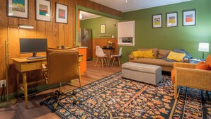 Una habitación con escritorio, silla, sofá, reposapiés y alfombra estampada.