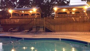 A swimming pool with a wooden deck and lounge chairs, surrounded by a wooden fence and a covered area with lights. - Pools, Hiking & Lake, Ping Pong, Shuffleboard!    Close to SDC, Lake, Shows (Branson West)