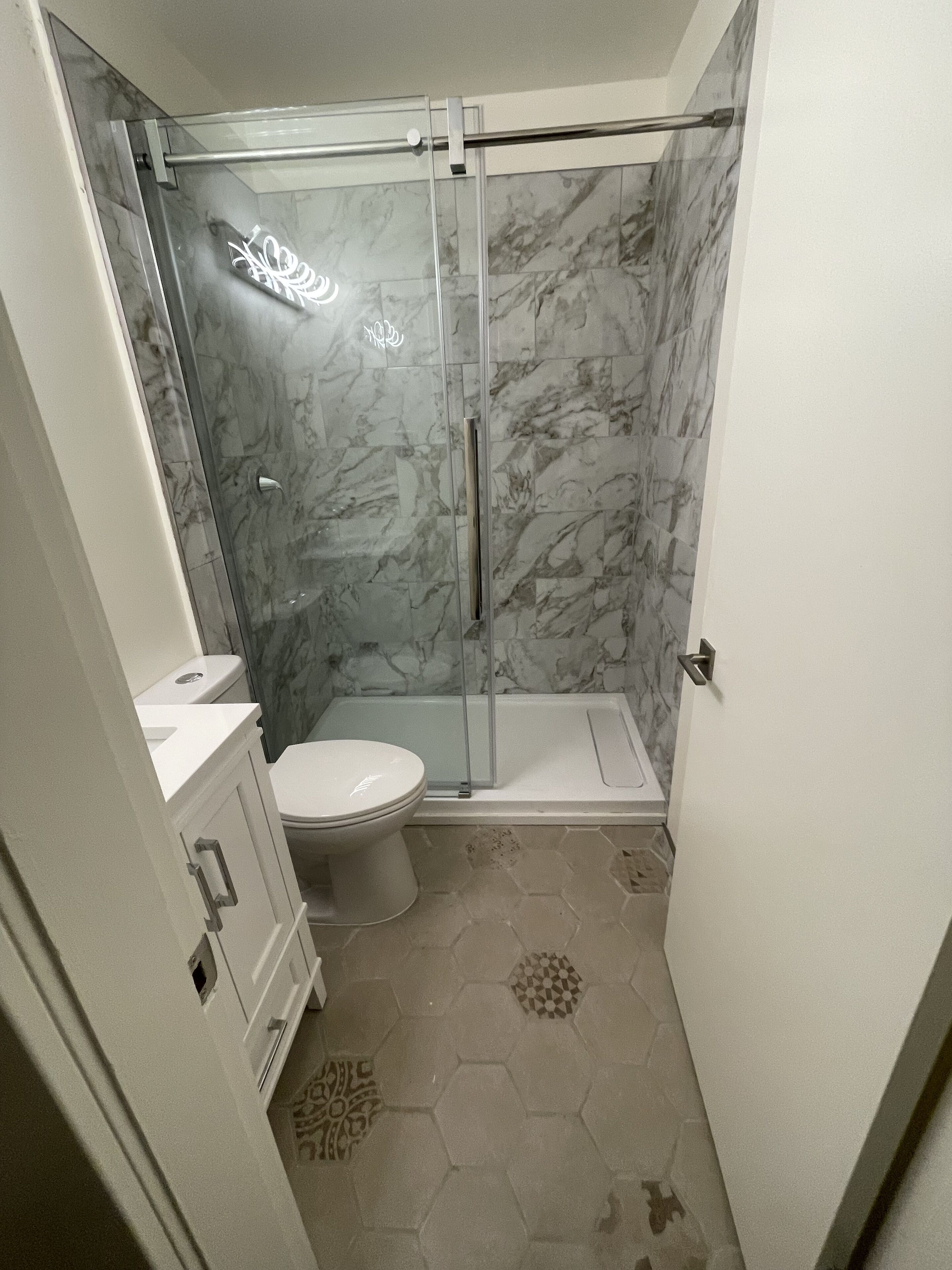 A bathroom with a glass-enclosed shower, a toilet, and a sink.