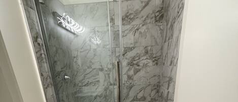 A bathroom with a glass-enclosed shower, a toilet, and a sink.