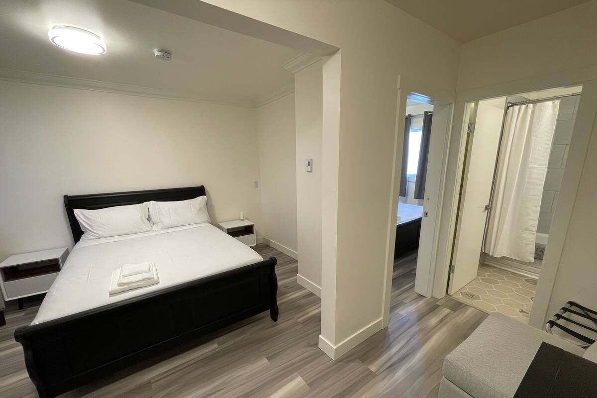 Un dormitorio moderno con una cama grande, mesitas de noche, un vestidor amplio y un baño visible a través de una puerta abierta.