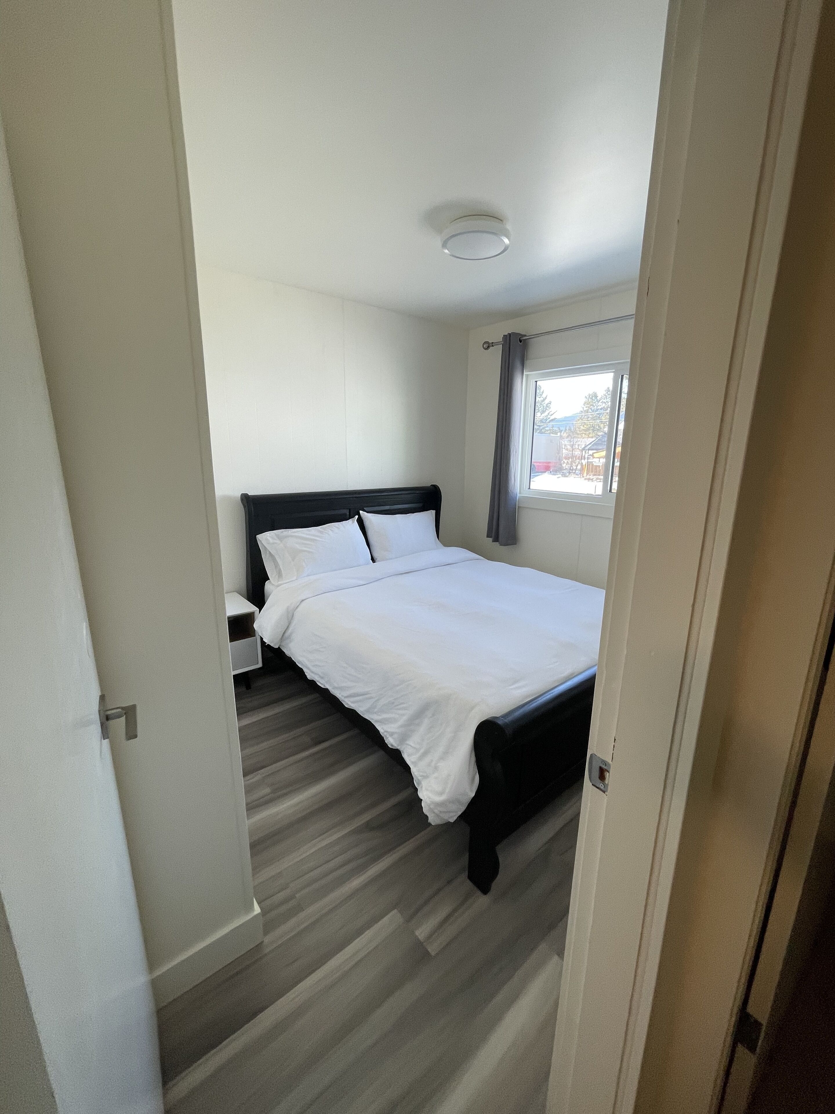 Une chambre d’hôtel avec un lit, une table de chevet, une fenêtre avec des rideaux et une porte.
