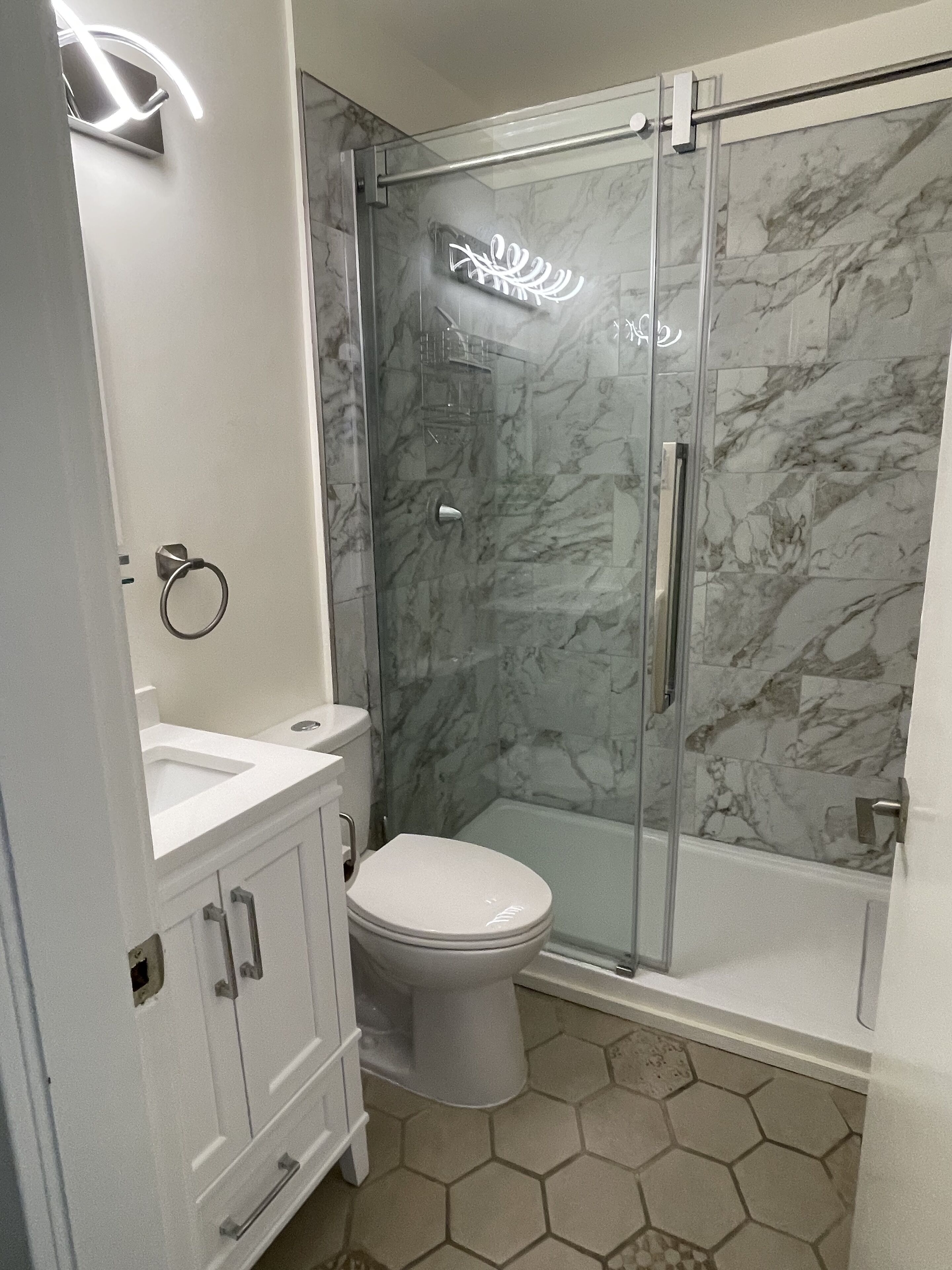 A bathroom with a glass shower enclosure, a toilet, and a sink.