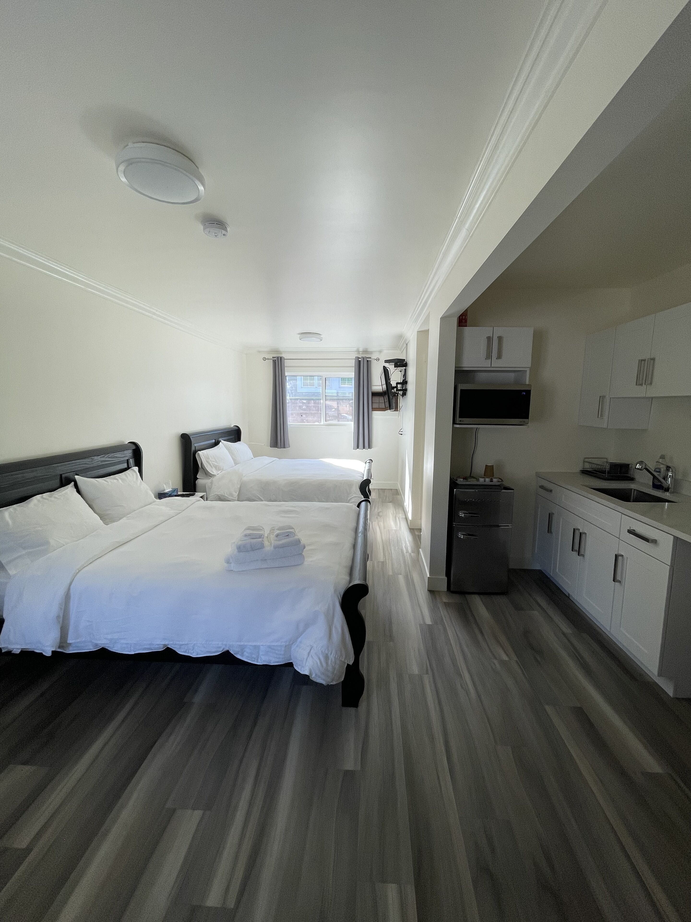 Une chambre d’hôtel avec deux lits, une kitchenette et une fenêtre avec des rideaux.