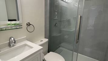 Ein modernes Badezimmer mit Duschkabine aus Glas, einem weißen Waschbecken mit Spiegel darüber und einer Toilette.