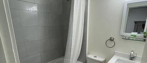 Ein modernes Badezimmer mit einer gläsernen Duschkabine, einer Toilette und einem Waschbecken mit Spiegel darüber.