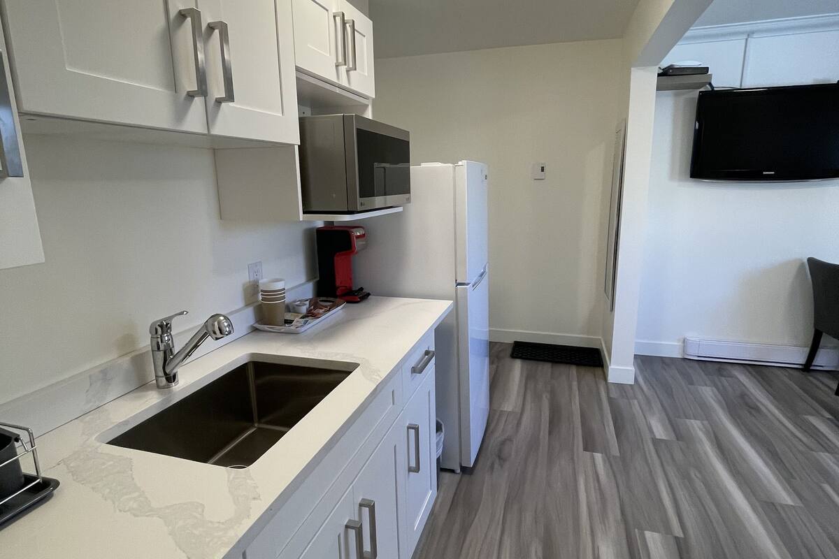 Una cocina compacta con alacenas blancas, un lavamanos de acero inoxidable, un microondas y un refrigerador.