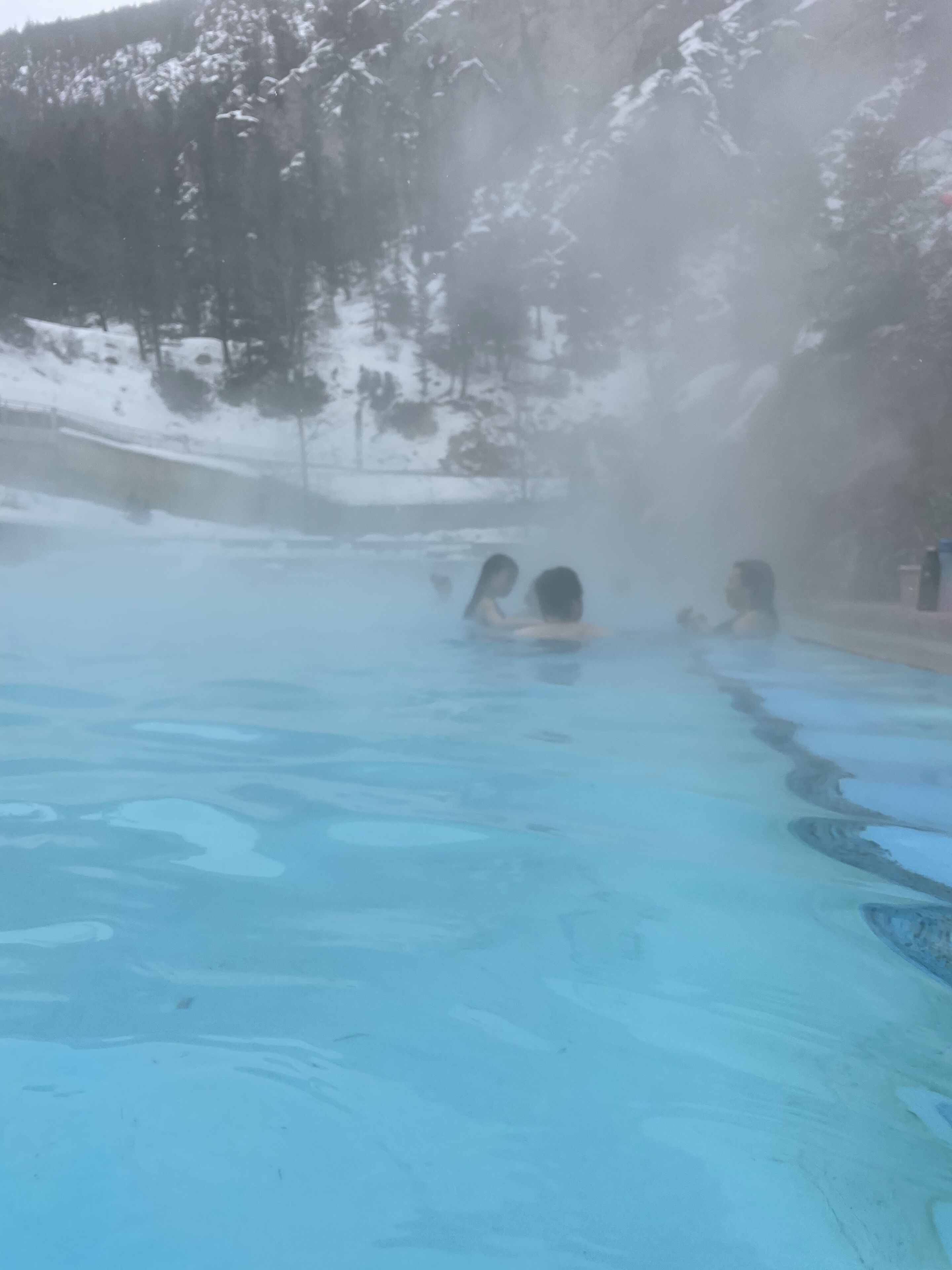 Un spa geotérmico con una piscina azul cristalina rodeada de montañas nevadas.
