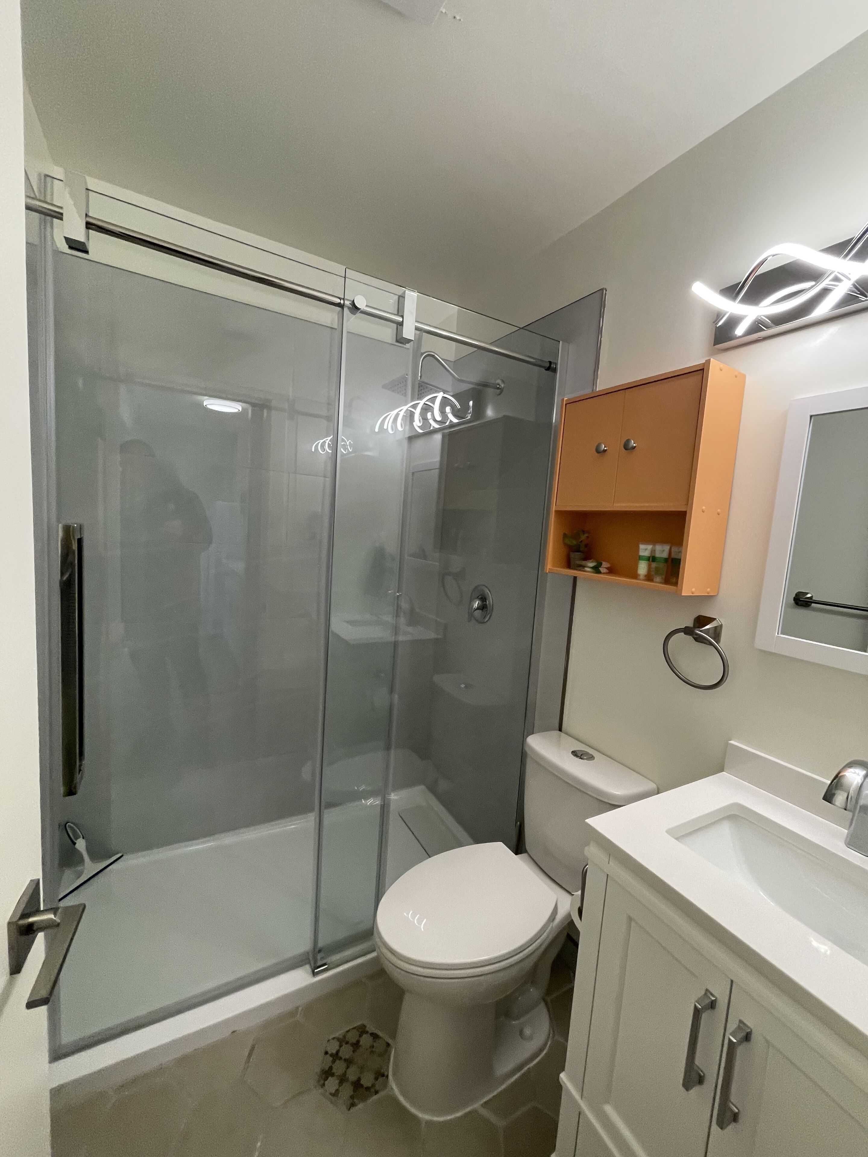 Ein modernes Badezimmer mit einer Glaskabine zur Dusche, Toilette, Waschbecken und einem Schrank.