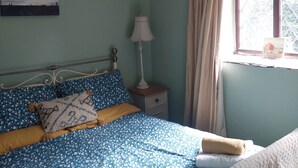 Een slaapkamer met een bed, een nachtkastje, een lamp, een raam met gordijnen en een hanglamp.