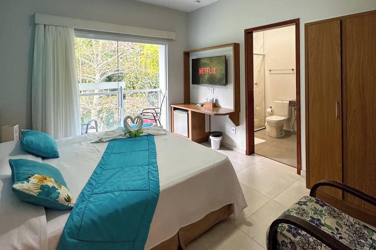 A hotel room with a bed, a TV, a desk, a bathroom, and a view of the outdoors.