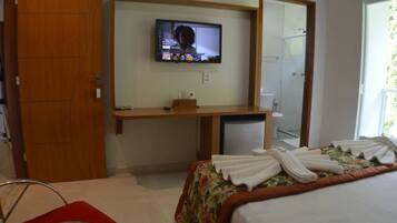Quarto de hotel com cama, escrivaninha com televisão, espelho e guarda-roupa.