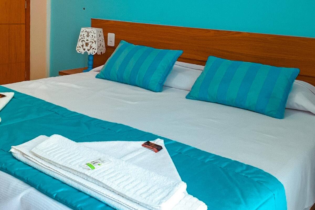 A neatly made bed with blue and white bedding, a wooden headboard, and a white lamp beside it.