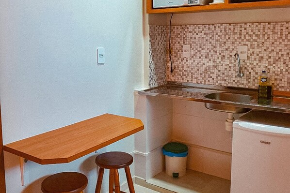 Una cocina compacta con encimera de madera, dos taburetes, un lavabo y un refrigerador pequeño.