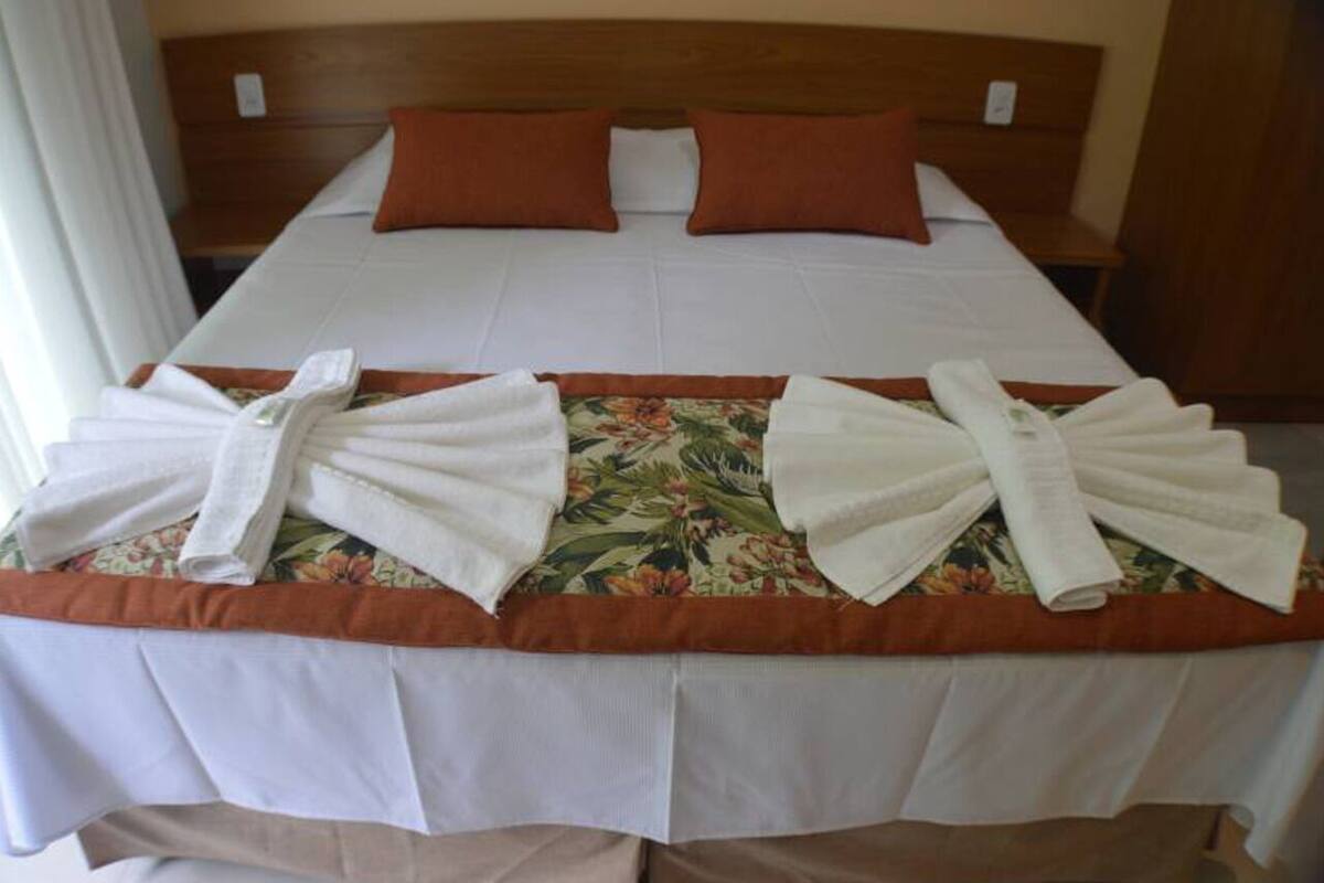 A neatly made bed with a floral bedspread, two pillows, and towels arranged on the bed.