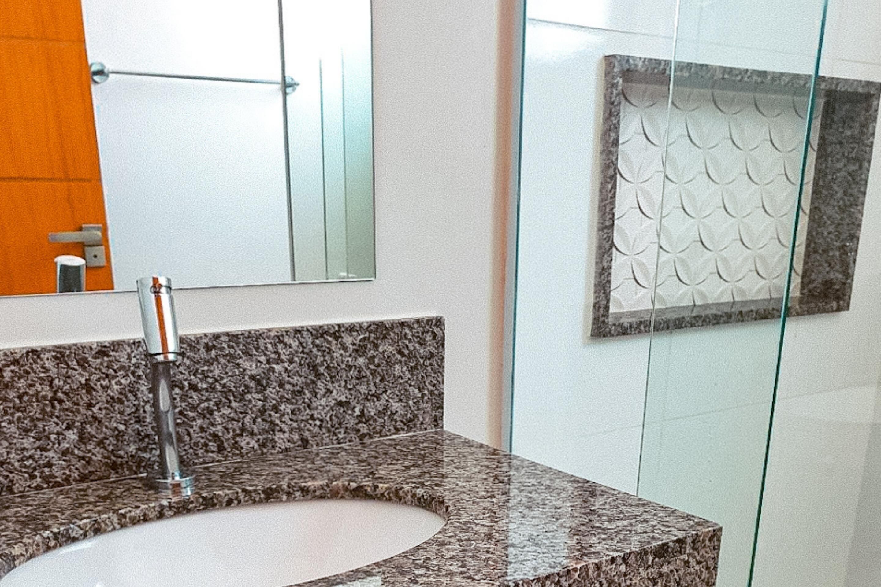 Un bany amb taulell de granit, un lavabo, un mirall i una cabina de dutxa de vidre.